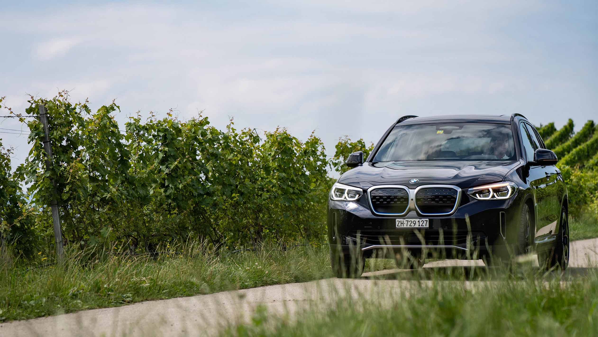 BMW iX3 nera su strada di campagna, vista frontale BMW iX3 nera su strada di campagna tra i vigneti