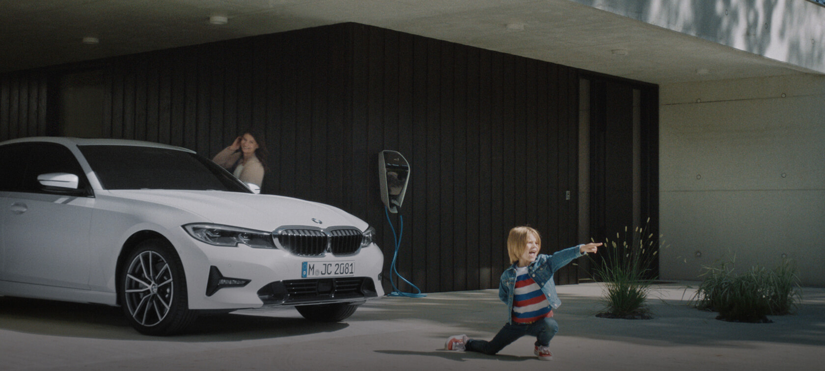 Femme avec enfant BMW Série 5 Berline Femme avec enfant/BMW/Série 5 Berline/blanc/de manière oblique et latérale depuis l’avant/parking avec borne de recharge/maison