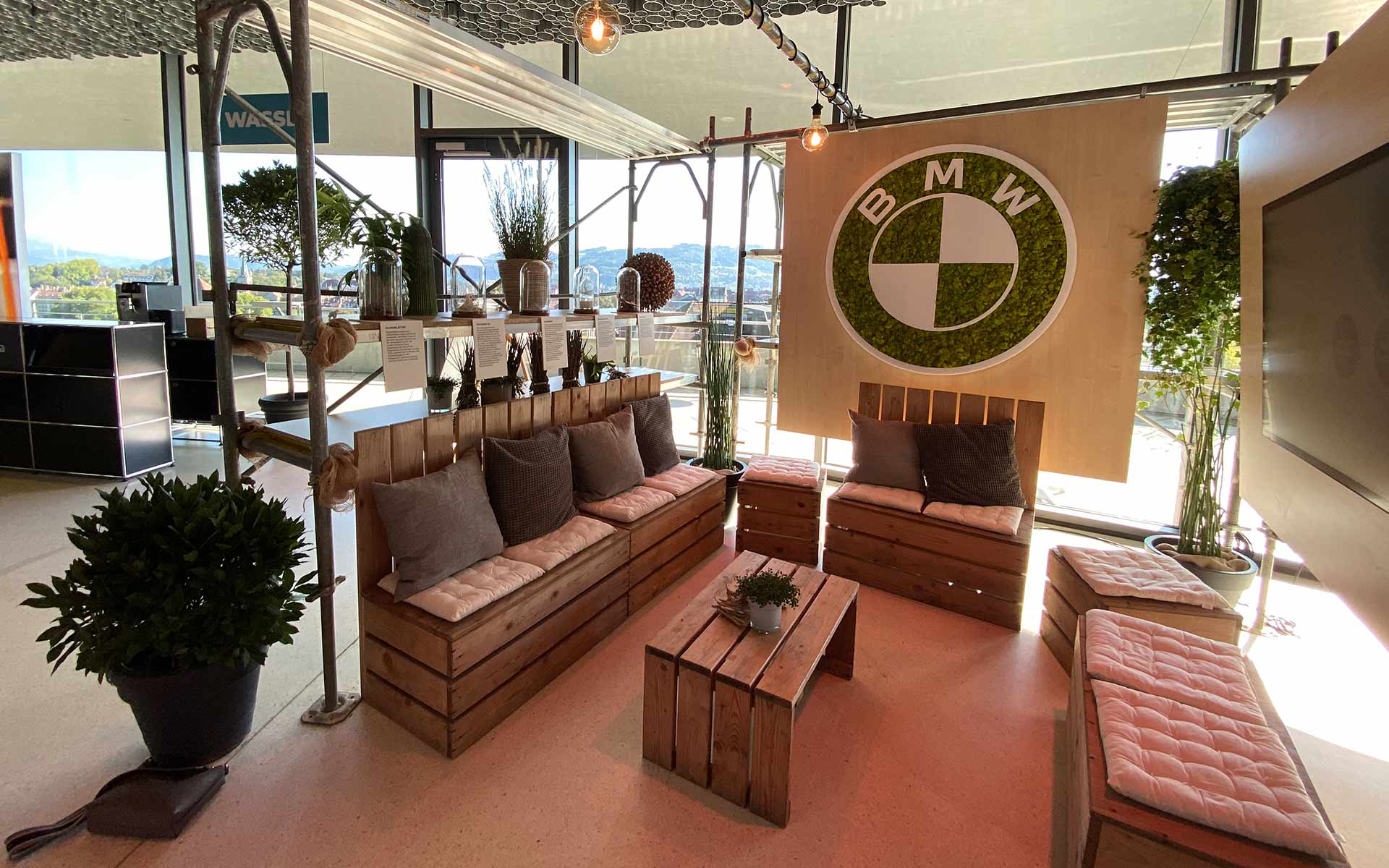 Stand de salon BMW avec grand logo BMW, coin salon convivial, plantes et écran plat