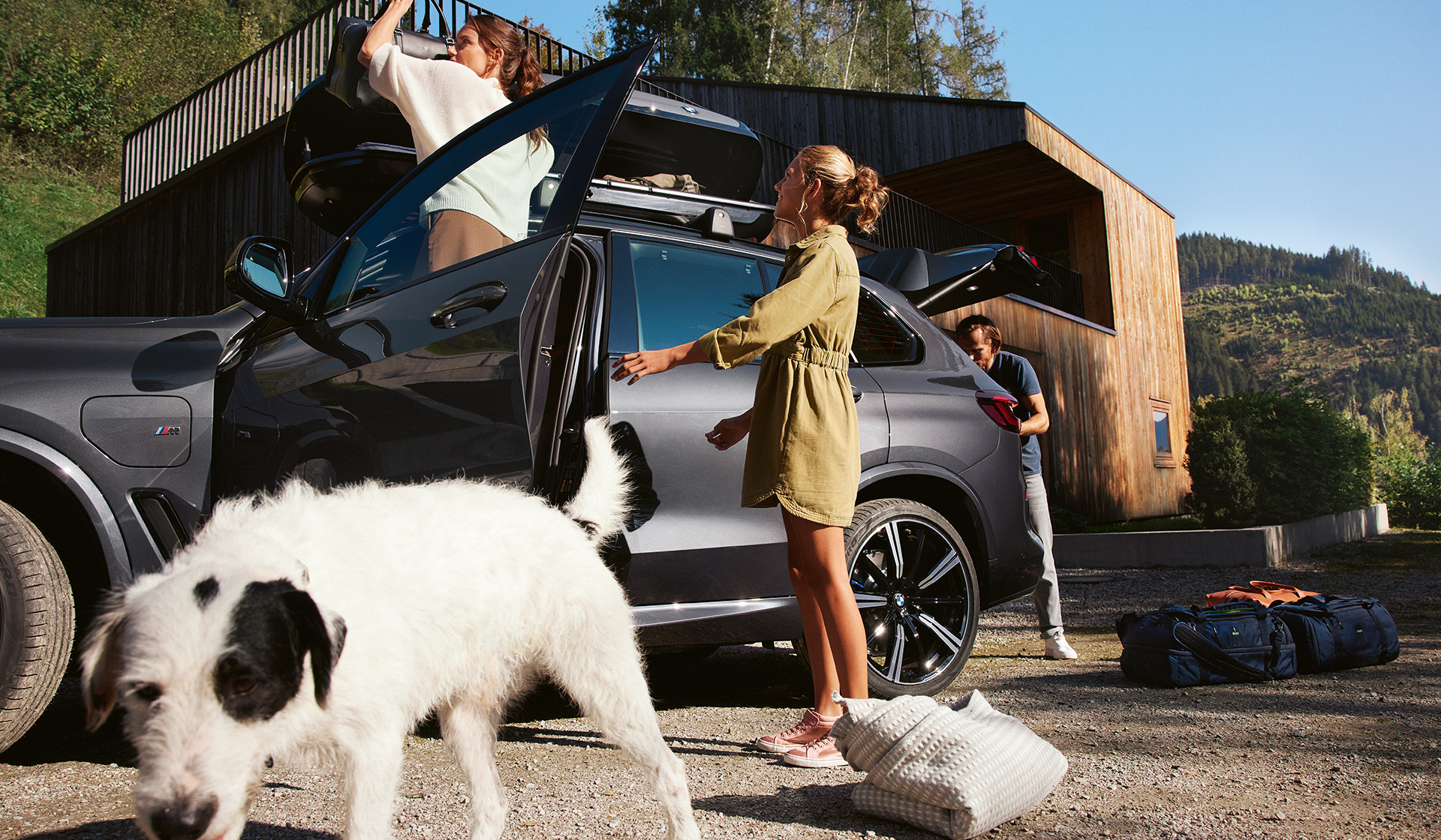 Hund vor Frauen und Mann beim Packen von BMW in Seitenansicht im Sommer BMW Feriencheck Hund vor Frauen und Mann beim Packen von BMW in Seitenansicht im Sommer