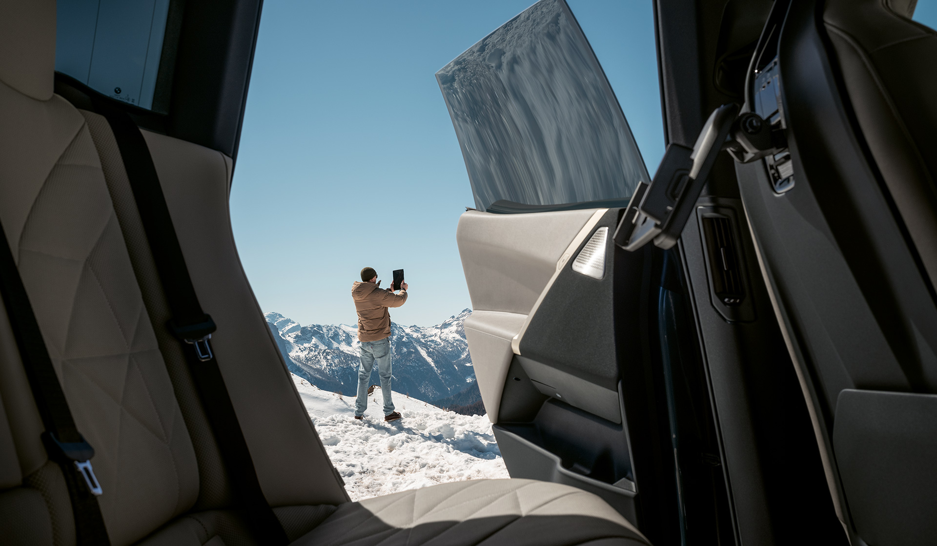 Blick aus BMW mit geöffneter Tür auf Person vor Bergpanorama im Winter BMW Feriencheck Blick aus BMW mit geöffneter Tür auf Person vor Bergpanorama im Winter