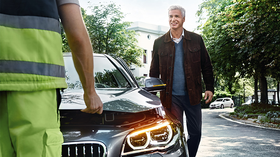 Dépanneur vu de dos posté devant un homme souriant à côté d’une BMW Dépanneur BMW vu de dos posté devant un homme souriant à côté d’une BMW vue de face