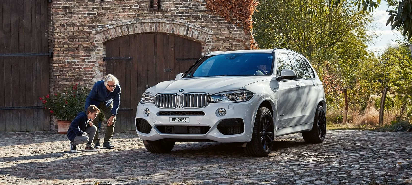 Mann mit einem Jungen BMW X5 xDrive 40e Mann mit einem Jungen BMW X5 xDrive 40e weiss seitlich von vorne Landhaus Parkplatz