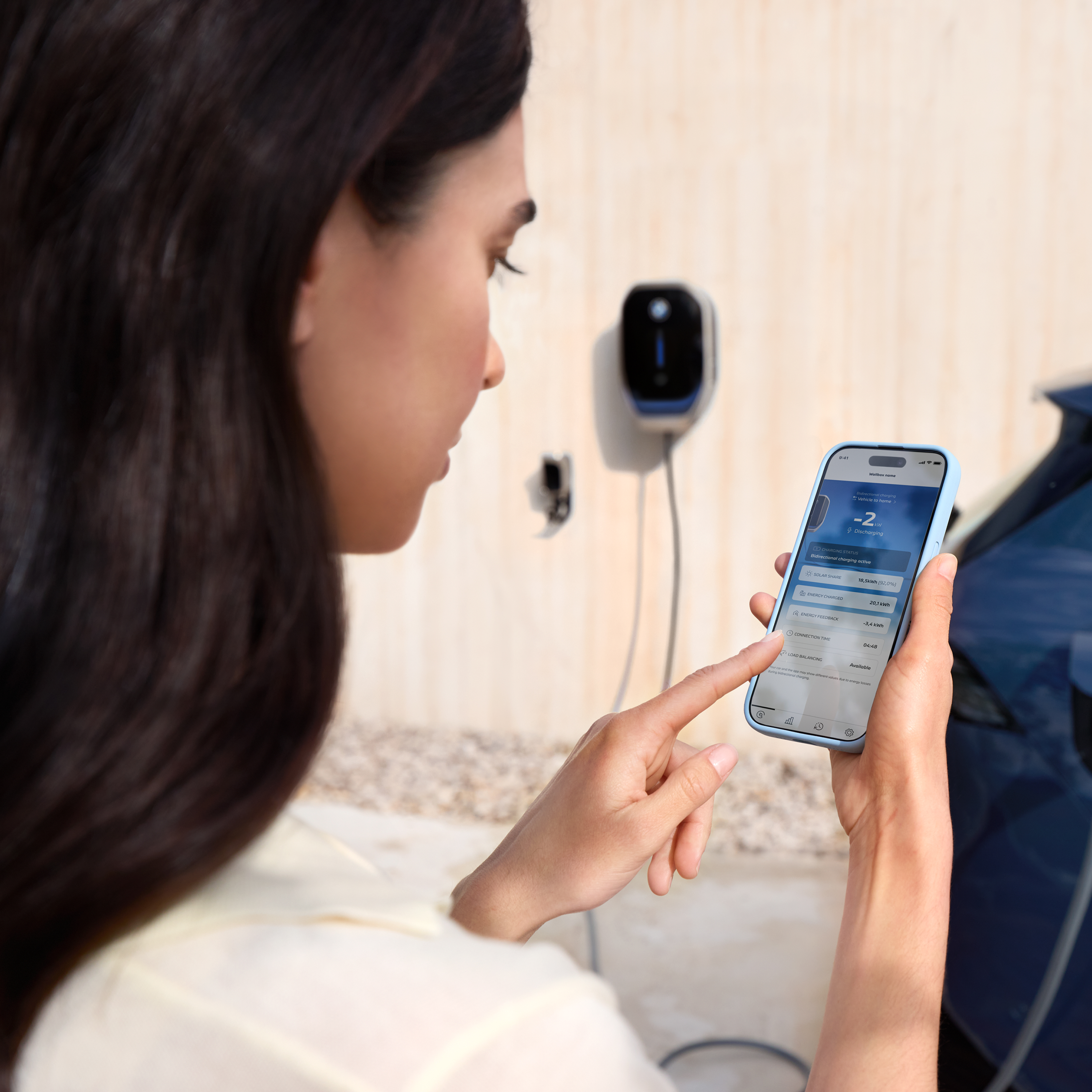 Una donna guarda il suo smartphone con una Wallbox BMW sullo sfondo
